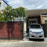 Koláž pěti fotografií z pronajatého domku v rezidenci Royal Garden na Nusa Dua, Bali. Zobrazuje sdílený bazén s lehátky, vjezd s autem a čistý interiér obývacího pokoje a dvou ložnic.