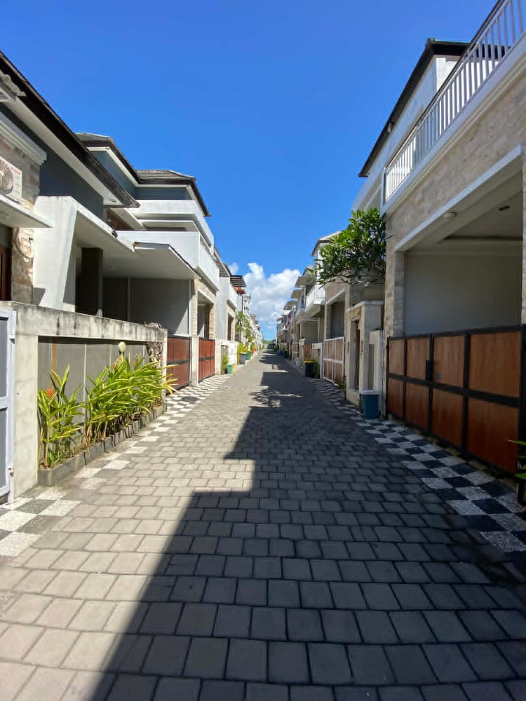 vysneny-dum-pronajem-sanur-bali.jpg Série fotografií exteriéru a interiéru čistého dvoupodlažního domu v bezpečné rezidenční čtvrti v Sanuru na Bali. Ukázka světlé ložnice, moderní koupelny a upravené ulice.